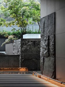 A dimly lit indoor space with a large stone wall, surrounded by modern design elements and natural ambiance from outside trees