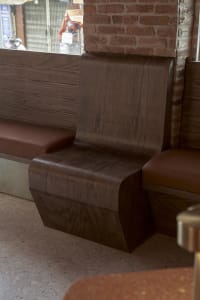 A room with a wooden bench and brick wall, featuring a brown leather seat and natural light from a window