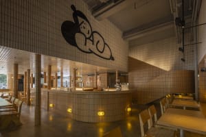 A restaurant interior with a counter and stairs, featuring a unique black and white mural on the walls, and comfortable seating areas with chairs
