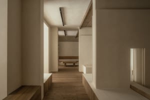 Empty white room with wooden floors and walls, featuring two benches and a calm atmosphere