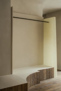 Empty room with a white wall, a wooden bench, and a doorway, giving a clean and minimalist appearance