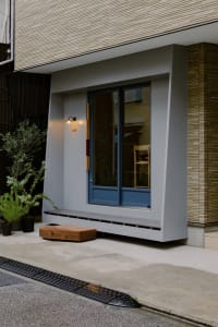A house with a large window on its side, two chairs in front, and a potted plant near the left chair, creating a calm and inviting atmosphere
