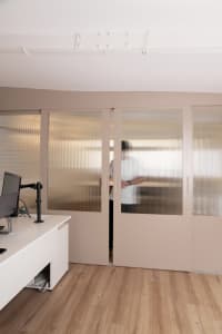 Office space with a wooden floor, natural light, and a man standing inside one of the rooms