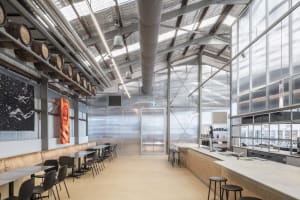 Industrial open space with a dining table and chairs, surrounded by a bar, with natural light coming in through windows or skylights