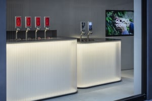 Modern bar area with white countertops, beverage dispensers, and cups, set in a stylish and upscale environment