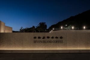 A coffee shop at night with a stone wall featuring embedded rocks and a sign reading Seventen Island Coffee, lit up against the dark sky
