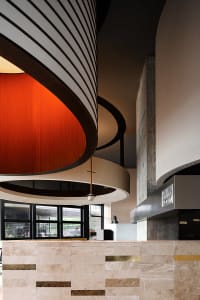 A modern lobby with a circular structure, dome ceiling, and a combination of wood and concrete walls, with natural light from multiple windows