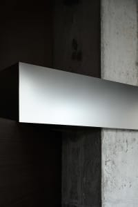 A dimly lit interior space with a large metal wall mounted on a concrete block, featuring a minimalist and contemporary style