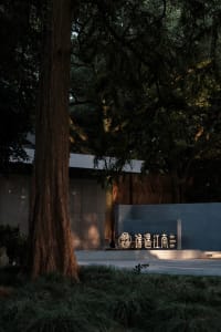 A serene Asian-style building with a stone wall and a large tree in front, featuring a modern concrete structure with a gray appearance