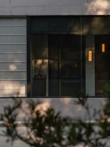 A modern building with a concrete exterior, featuring a doorway with a glass window and two windows on either side, under daytime lighting