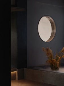 A calm bathroom with a large mirror above a sink, surrounded by two potted plants and a sense of serenity