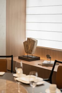 A warm and inviting dining space with a wooden table, chairs, wine glasses, a book, and a sculpture, creating a stylish and comfortable environment