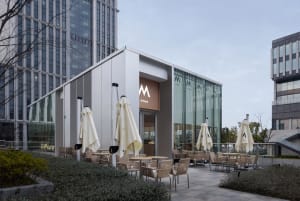 A modern restaurant with a glass wall, umbrellas, and outdoor seating with dining tables and chairs