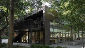 A wooden building with a large glass window, surrounded by chairs in a calm and inviting public space with natural light