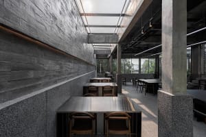 A modern restaurant interior with grey stone walls, numerous dining tables, and comfortable seating
