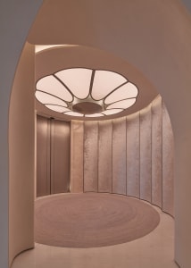 A warm hallway with pink and white walls, a wooden circular design element, and a doorway leading to another part of the building