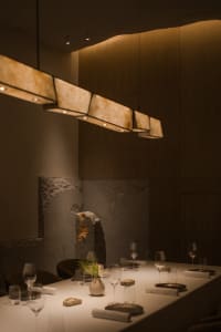 Elegant dining area with a long wooden table, chairs, wine glasses, and cups, set for dinner in a sophisticated atmosphere