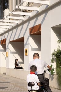 A daytime photo of a building with a wooden bench and natural light, featuring two people in the scene