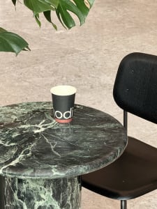 A modern indoor space with a marble table, a black chair, two cups, and a potted plant, featuring a sophisticated atmosphere