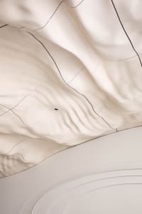 A modern interior space with a white ceiling featuring a wave-like pattern made of fabric, creating a contemporary atmosphere