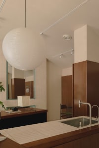 Modern bathroom with a sink, mirror, and a large white ball hanging from the ceiling, accompanied by two chairs and a minimalist design
