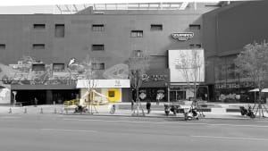 Busy city street scene with a building featuring a yellow box on its side, pedestrians, and parked motorcycles