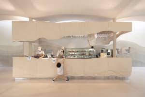 A lively restaurant interior with a modern design featuring wood elements, people standing at the counter, and a child climbing on the counter
