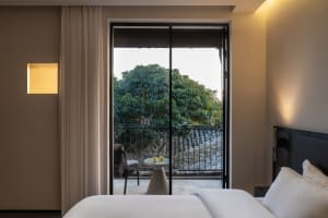 A calm bedroom with a large window, two chairs, a dining table, and a couch, flooded with natural light from outside