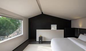 A modern bedroom with two beds, a chair, and a large window allowing natural light to enter the space
