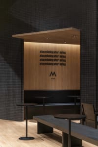 Modern restaurant interior with wooden walls, black tables, and a bench providing seating options