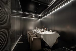 A sophisticated dining area with a long wooden table, multiple chairs, wine glasses, vases, and potted plants, perfect for special events or intimate gatherings