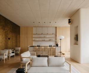 Open living area with wooden floors and walls, featuring a couch, dining table, and kitchenette, with decorative vases and ample seating options