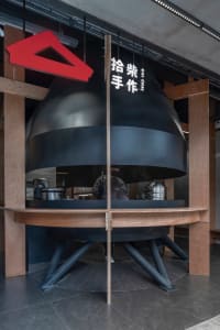 A modern Asian restaurant with a large black oven, wooden tables, and chairs, creating a warm and inviting atmosphere