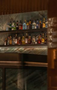 A bar area with a glass bottle display on a shelf, featuring a variety of liquor bottles in different sizes and shapes