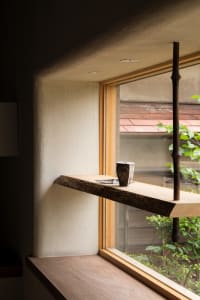 A room with a wooden shelf, a cup, and two potted plants, lit by natural light from a window