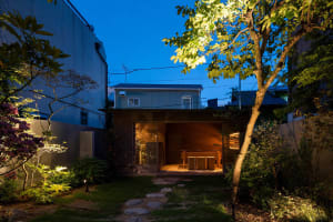 A cozy outdoor dining space with two tables and chairs on a patio, illuminated by night lights