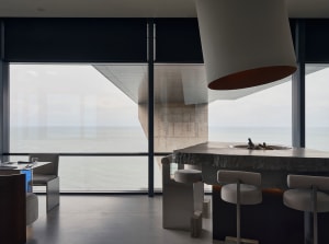 Open modern living space with a kitchen island, stools, chairs, and a large window providing natural light, featuring a marble countertop