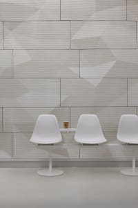 Modern dining area with two white chairs and a small table in front of a wall with a unique brick pattern design