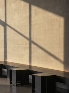 A dimly lit room with a cement wall, a window, and three wooden benches placed along the wall