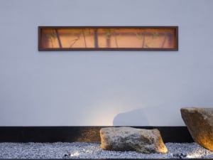 A modern space with a rock wall featuring a window and two rocks, a bench, and a bright atmosphere