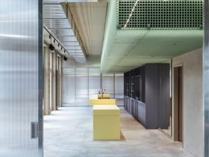 Office space with a yellow countertop, two sinks, and a large window allowing natural light to enter, set against concrete walls