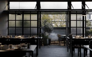 A restaurant with dining tables, chairs, and decorative items, illuminated by natural light through a large window