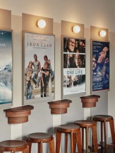 A casual space with a row of wooden stools against a wall, accompanied by three posters on the wall above, creating a welcoming atmosphere