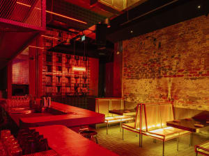 A warm and inviting bar area with red walls, chairs, a dining table, and bottles, perfect for socializing and enjoying meals