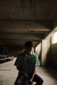 A man stands in a room with a concrete wall and cement floor, giving it an industrial feel