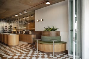 A cozy cafe with a round table surrounded by chairs, potted plants, and modern tiled walls