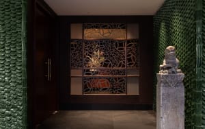 Elegant hallway with a door, glass wall, and display cases showcasing artwork and a potted plant, set against a tasteful backdrop