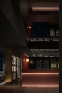 A sophisticated bar area with a long countertop, wine glasses, and bottles, set against a backdrop of red walls and wooden accents