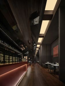 A modern restaurant interior with a bar area featuring a counter and bottles, surrounded by dining tables and chairs, on a wooden floor
