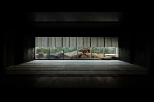An empty room with large windows, natural light, and several rocks arranged within the space